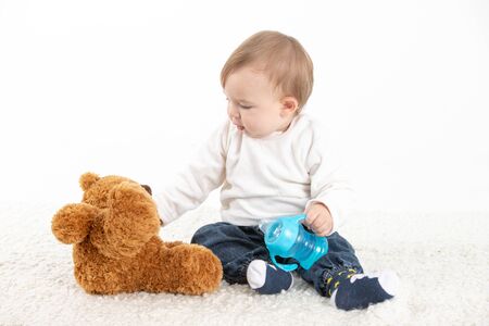 Stock studio photo with a white background of a baby sitting with a canteen with handles and a teddy bear.の写真素材