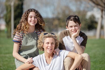 Family made up of a mother, son and daughter pose on a sunny day in a public park with a very affectionate attitude.の写真素材