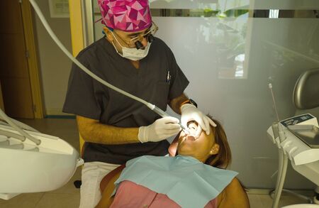 Dentist opens the mouth of his patient and begins to revise the interior helped by his instrumentsの写真素材