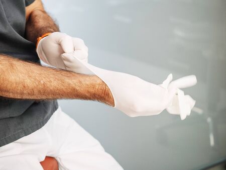Doctor puts on latex gloves before proceeding to perform his workの写真素材