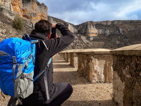 Photographer with a blue bag crouching in the middle of a sandy path taking a picture in the middle of the mountain surrounded by rock formations in Maderuelo in Spainの写真素材
