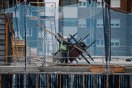 April, 15 2020, in Madrid, Spain a worker carries a heavy wooden slat in a building. Always protected with a mask from the covid 19のeditorial素材