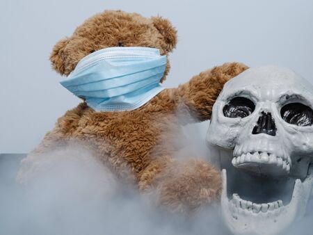 Teddy bear and open-mouthed skull with covid 19 coronavirus mask surrounded by smokeの写真素材