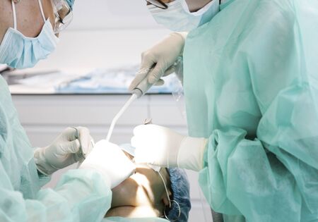 From below female dentists in uniform using professional tools to do surgery on anonymous patient during work in modern clinicの写真素材