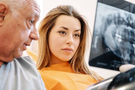 Dentist speaking with young woman while sitting near computer during appointment in contemporary clinicの写真素材