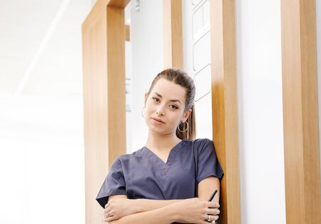 Young, beautiful nurse in blue uniform waits in the doctor's office hallwayの写真素材