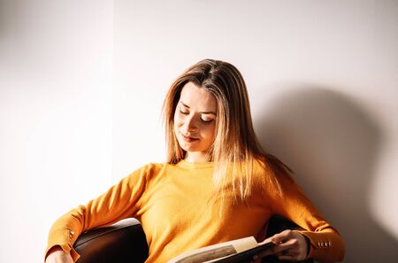 Young female patient smiling and reading magazine while sitting in armchair against white wall and waiting for appointment in clinicの写真素材