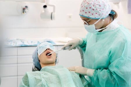 Dentist assistant inserts tool in patient's mouthの写真素材