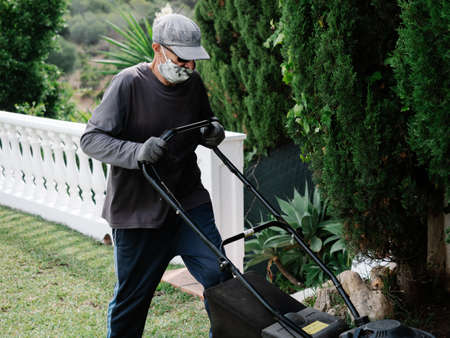 person with mask is preparing the garden with an electric mowerの写真素材