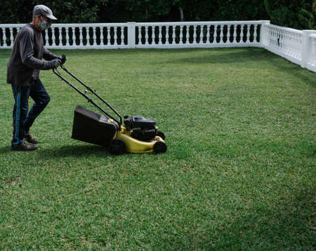 person with mask is preparing the garden with an electric mowerの写真素材