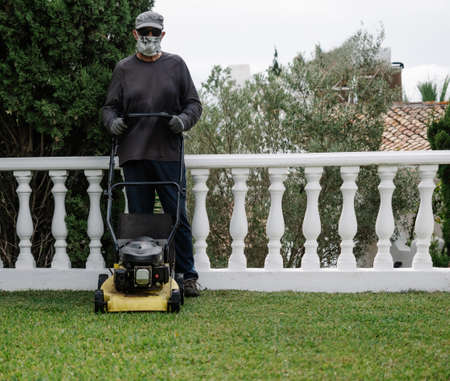 person with covid mask poses next to his mower before preparing the gardenの写真素材