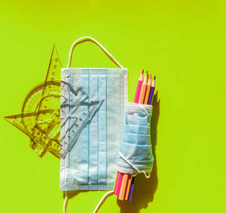 Set of colored pencils wrapped in a hygienic mask, next to another mask and next to materials such as ruler, bevel and square. School material against covid 19の写真素材