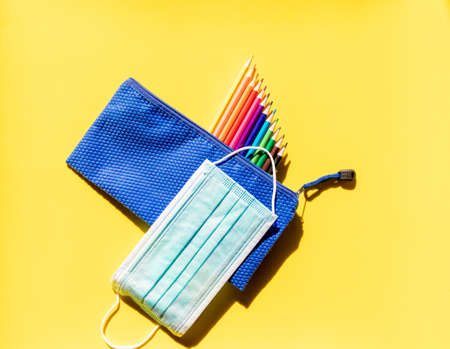 Back to school. Colorful image with children's case, color pencils and mask against covid 19の写真素材