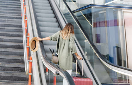 Back view of anonymous woman with suitcase waving hand with hat and walking on platform of railroad station during summer vacationの写真素材