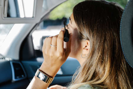 Crop female with pocket mirror pouting lips and applying rouge on cheek while sitting on passenger seat of vehicleの写真素材