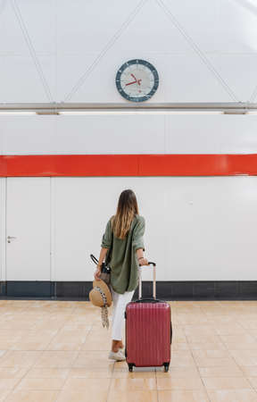 Back view of anonymous woman with suitcase waving hand with hat and walking on platform of railroad station during summer vacationの写真素材
