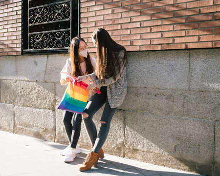 Content lesbian females standing together near building on street with rainbow LGBT bag and looking at each otherの写真素材