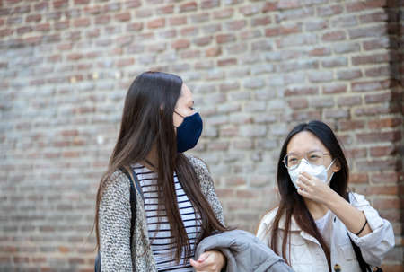 Delighted multiethnic female friends wearing protective masks walking in Madrid and enjoying weekend together during coronavirus epidemicの写真素材