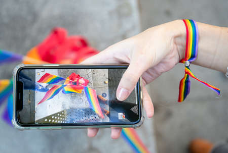 Top view of crop anonymous female in rainbow bracelet taking photo of LGBT flags while using smartphone on streetの写真素材