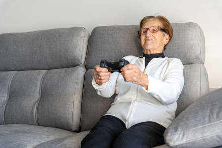 Cheerful aged female sitting on couch at home and speaking on video chat with family on mobile phoneの写真素材