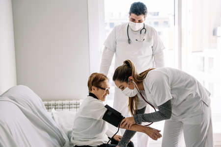 Doctors in medical masks using tonometer and measuring blood pressure of elderly female patient...