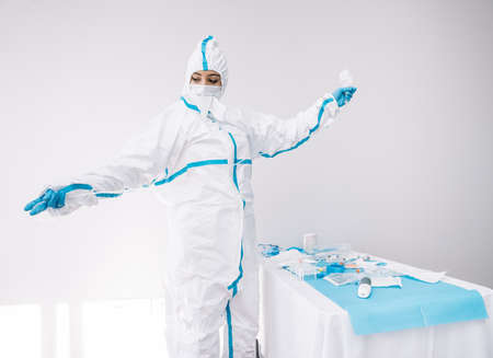 Medic in protective mask and uniform standing with colleague in medical room and using dropper while working in clinic during COVID 19 pandemicの写真素材