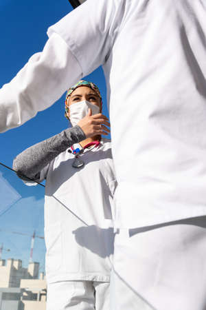 Low angle of female doctor in uniform standing on balcony with coworker and relaxing during working dayの写真素材