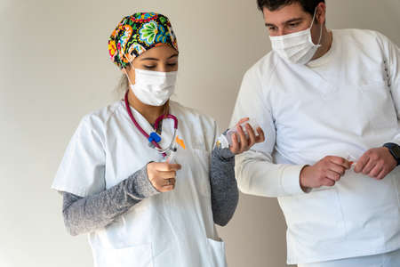 Delighted female doctor with syringe and in protective mask standing in medical room with male colleagueの写真素材