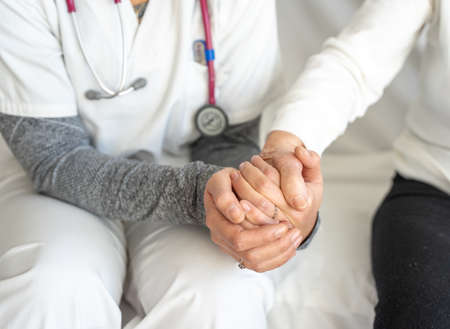 High angle of crop anonymous medic holding hand of senior female while sitting together on couchの写真素材