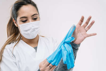 Female medic in protective mask taking off used latex gloves after work in clinic during  pandemic