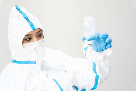 Female medic in mask and protective costume standing with dropper in white room while working duringの写真素材