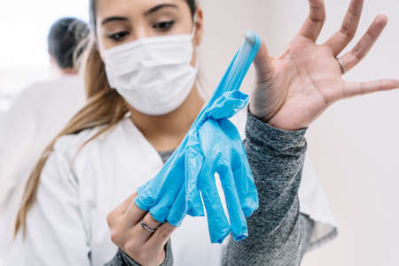 Female medic in protective mask taking off used latex gloves after work in clinic
