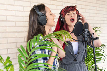 Young female vocalists singing with closed eyes near microphone during performance near green plantsの写真素材