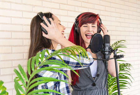 Young female vocalists singing with closed eyes near microphone during performance near green plantsの写真素材