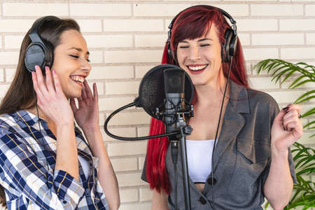 Happy young women with headset standing near microphone and enjoying singing against brick wall and plantの写真素材