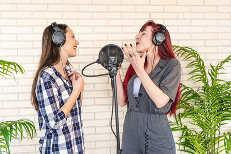 Young women with closed eyes gesticulating and singing into microphone while listening to music in headphones in light professional studioの写真素材