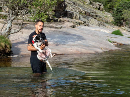 Close-up of dog trainer holding puppy to teach him to swim in a lake. Black and white puppy learning to swim in a lake.の写真素材