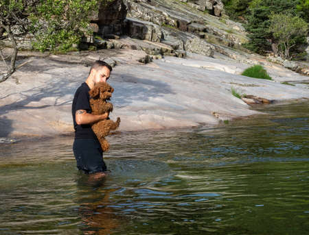 Close-up of dog trainer holding woolly puppy to teach him to swim in a lake. Brown puppy learning to swim in a lake.の写真素材