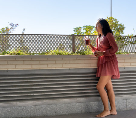 barefoot woman standing resting with a fruit juice in hand, horizontal close up with the sky in the backgroundの写真素材