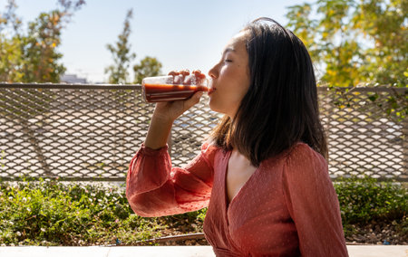 woman drinking a glass of a fruit smoothie, looking to the side, horizontal side viewの写真素材