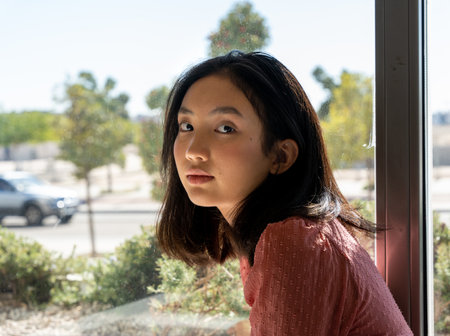 portrait of an Asian woman looking at the camera next to the window, horizontal urban backgroundの写真素材