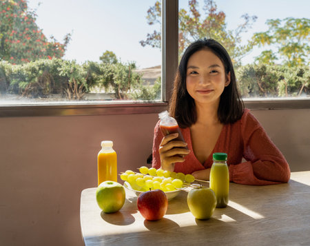 young woman posing seated with a table full of fruit and smoothies, natural landscape in the backgroundの写真素材