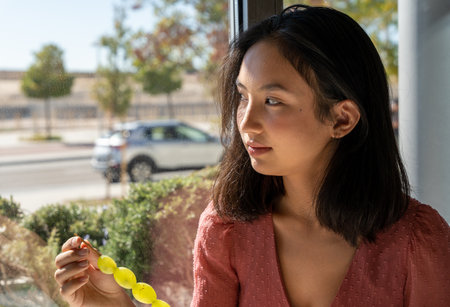 distracted woman looking out the window while eating grapes, horizontal urban backgroundの写真素材