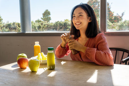 smiling woman opening a healthy fruit smoothie, sitting and receiving the sunlight, horizontal close upの写真素材