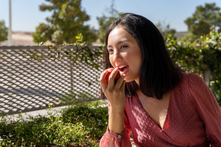 woman bringing an apple to her mouth to take a bite, close-up view, receiving sunlightの写真素材