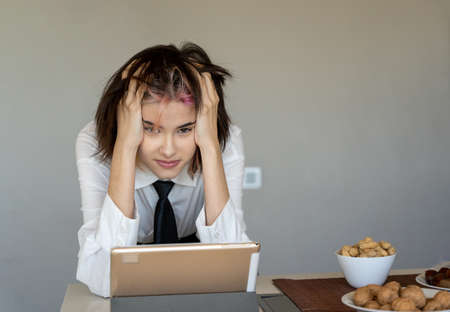 woman with her hands on her head frustrated in front of her tablet, staring at the cameraの写真素材