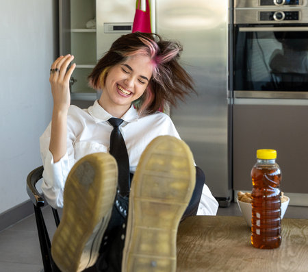 happy woman shaking her head from side to side, reclining in her chair with her feet on the worktop, horizontal indoor pictureの写真素材