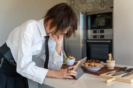 executive woman looking at a recipe on a tablet, standing in the kitchen, horizontal pictureの写真素材