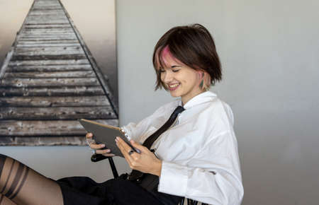 smiling woman in shirt and tie reclining in a chair looking at her tablet, side horizontal viewの写真素材