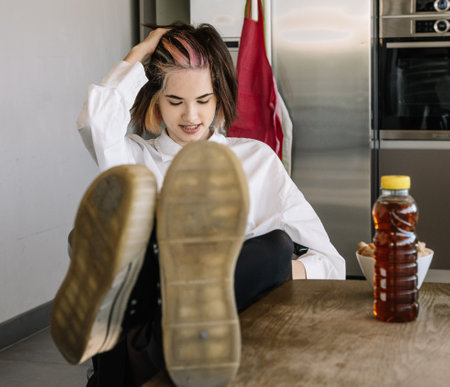 front view of a girl sitting with her feet on the kitchen table next to a bottle of soda, horizontal viewの写真素材
